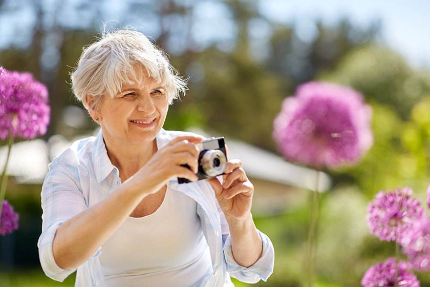 Senior woman with camera photographing flowers 